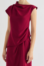 A luxurious 4-ply silk top in  wine color, featuring a hand-draped neckline styled in an elegant, scarf-like fold. The silk fabric shines softly under the light, highlighting its rich texture and versatility. The top is paired with coordinating silk trousers, creating a sophisticated and timeless look.