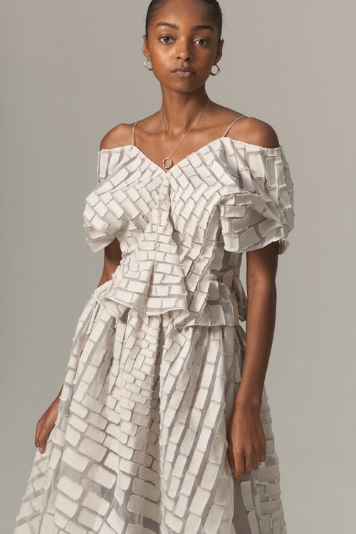 A woman wearing an off-shoulder top with a geometric brick pattern in ivory, vintage blue, and dove colors.